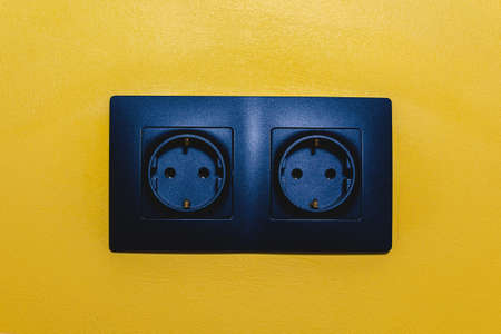 Dual electrical outlet on yellow wall. Electricity consumption in homes and offices. Safety of using electrical outlets. Modern sockets as an interior decoration.の写真素材