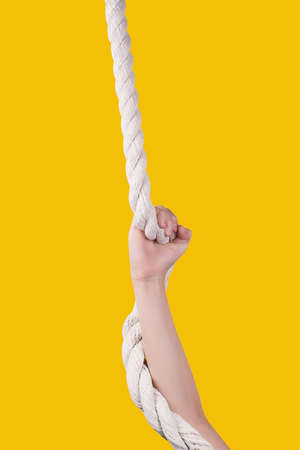 Kid's hand on white rope on vivid yellow background. Child resistance. Work hard and make efforts...