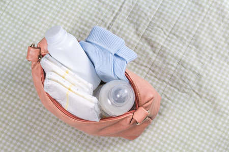 Small pink diaper bag on changing pad. First care baby accessories with bottle. Soft green background. Top view. Newborn and maternity concept.の写真素材