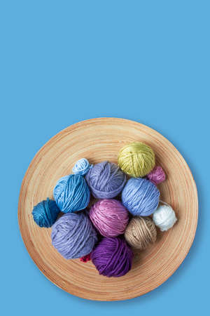 Funny multicolored woolen balls in wooden bowl on blue background. Top view. Close up. Knitting as hobby. Copy space. Vertical format.の写真素材