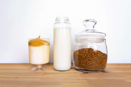 Ingredients for Dalgona coffee. Instant coffee and milk in glass jars on wooden table. Iced dalgona...
