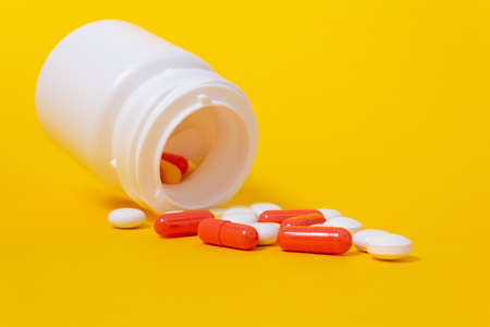 White pills and red ampules falling from plastic medicine jar. Bright yellow background. Minimalistic medicine and healthcare concept. Pharmaceutical medicine pills, tablets. CLose up.の写真素材