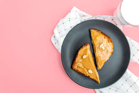 Top view. Peanut butter toasts on matte trendy dark blue plate with whole peanuts and milk in glass. White napkin and soft pink background. Copy space.の写真素材