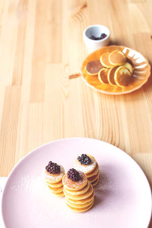Trendy tiny pancakes cereal meal on pink plate. Baked pancakes for breakfast on wooden background. Fresh berries for decoration in background.の写真素材