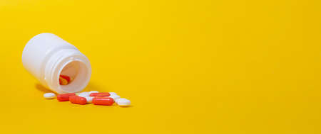 Banner with white pills and red ampules falling from plastic medicine jar. Bright yellow background. Healthcare concept. Pharmaceutical medicine pills, tablets. CLose up. Copy space.の写真素材