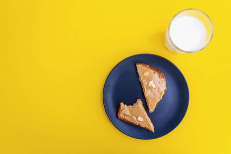 Top view. Peanut butter toasts on matte trendy dark blue plate with whole peanuts and milk in...
