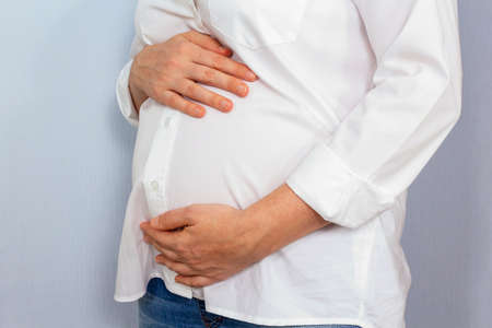 Unrecognizable caucasian middle aged pregnant woman in white shirt holding tummy, showing care for her and baby. Long-awaited pregnancy.の写真素材