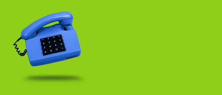 Vivid blue old landline phone on green background. Banner. Copy space. Hotline phone, call center,...