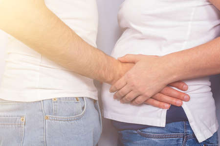 Husband hugging wife's pregnant belly. Minimalism lifestyle. Amazing toned photo with sun light and...