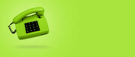 Vivid green old landline phone on green background. Banner. Copy space. Hotline phone, call center, customer service help desk or contacts on site. Levitation and monochrome concept.の写真素材