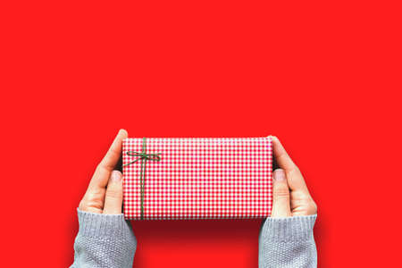 Small present in red gift box in woman hands in cozy gray sweater. Craft paper decorated with green...