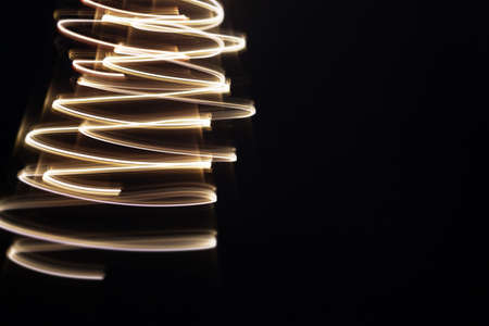 Christmas tree from golden light lines on black background. Copy space. Christmas tree illusion . Glamorous glowing greeting card.の写真素材