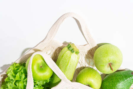 Top view of fresh green vegetables and fruits in string bag on light background. Salad, apples and...