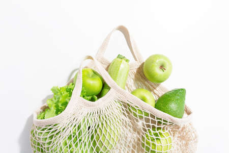 Top view of fresh green vegetables and fruits in string bag on light background. Salad, apples and...
