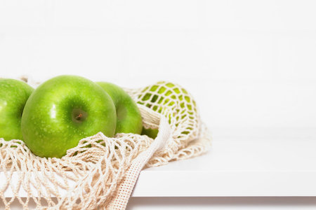 Green apples in eco mesh bag on white kitchen table. Market shopping. Food and Environment concept. Zero waste. Copy space. Close up.の写真素材