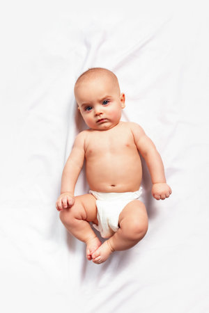 Caucasian funny child in white nappy lies on light background. Top view. Childrens hygiene, nappy...