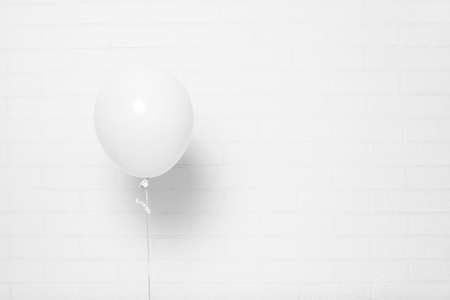 White helium balloon on white brick wall. Copy space. Can be used as mock-up.の写真素材