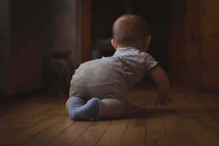 Little funny baby boy learning to crawl on wooden floor. Selective focus. Rear view. Family life.の写真素材