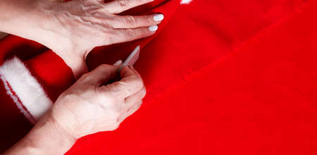 Grandma sewing small Santa hat for grandchildren. Close up. Tailor's chalk in hands to make sewing...