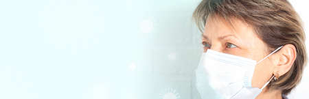 Elderly caucasian woman wearing Medical Face Mask and looking to the left. Banner format. Medical blue background with drawn viruses. Copy space.の写真素材