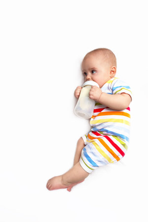 Cute caucasian baby with first baby milk bottle. Top view. Artificial feeding concept. Baby milk formula. Infant in striped jumpsuit on white blanket.の写真素材
