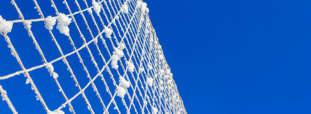 Volleyball net covered with snow against blue sky on clear winter day. Natures minimalism. Banner format.の写真素材