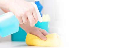 Woman cleaning table with blue color disinfectant spray and yellow towel. Banner with white copy...