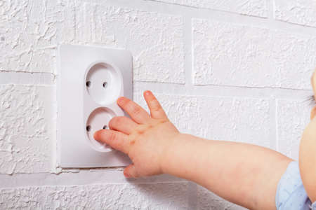 Baby small hand near electrical socket. Unrecognizable caucasian baby boy is playing with open...
