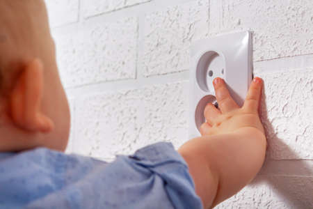 Unrecognizable caucasian boy is playing with open electrical outlet. Baby wires. Dangerous games...