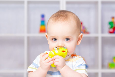 Cute caucasian baby boy in striped bodysuit playing with yellow plastic cat. Different childrens...