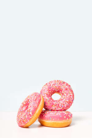 Cute fresh pink donuts in stack. Vertical format. Copy space on top. Light blue background. Donut day celebration.の写真素材