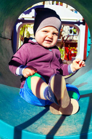 Cute little caucasian boy sitting at children's play complex. Baby sits inside blue plastic tubein....
