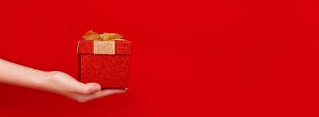 Valentine delivery banner. Gift box with golden bow on hand. Red beckground. Gift in hand. 14 February gift. Valentines day present from teenager.の写真素材