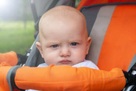 Funny caucasian baby boy sitting in stroller durind walk and making very serious face. Summer day....