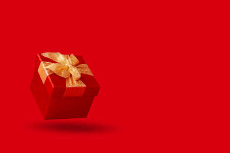 Amazing red gift box with golden bow. Levitation on red background. copyspace. Christmas present. February 14 or Saint Valentine day.の写真素材