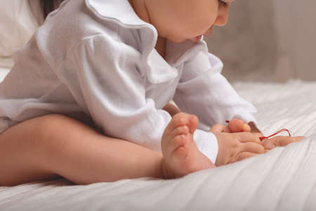 Little caucasian baby girl playing with red thread on little hand. Talisman for baby. Protection...
