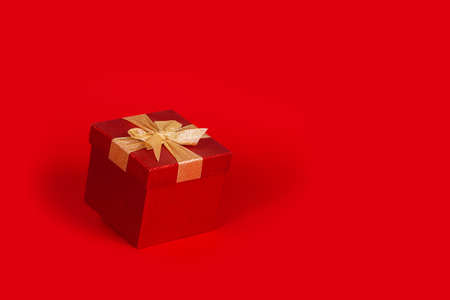 Amazing red gift box with golden bow. Right copy space on red background. Christmas present. 14 February or Saint Valentine day.の写真素材