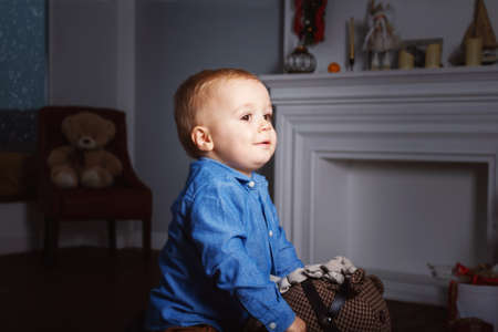 Caucasian adorable baby boy sitting on toy horse in his room and playing in the evening. Snowing....