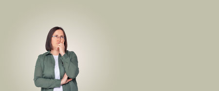 Young brunette woman with short hair and glasses thinking. Woman in contemplation. Banner format. Neutral color background. Right copy space.の写真素材