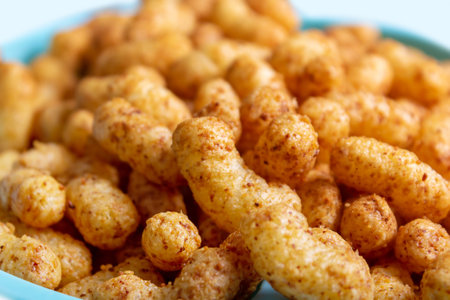 Puffed corn peanuts snacks served on blue plate. Close-up. Selective focus. Cheese flavored puffed...