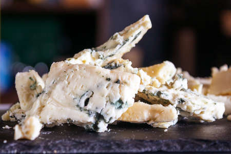 Cheese store. Crumbly blue mold Roquefort cheese on black stone board. Selective focus. Close up.の写真素材