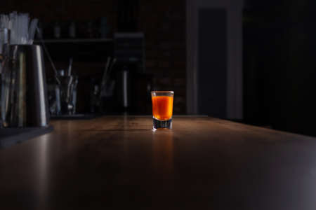 Orange colored alcoholic shot in glass shot glass on wooden bar. Orange cocktail. Lonely night at the bar. Loneliness and desire for drink. Brutal cocktail.の写真素材
