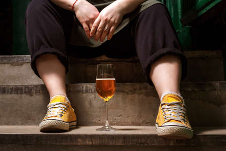 Unrecognizable caucasian woman in yellow sneakers sitting on stairs with cider. Small grocery store...