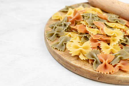 Top view of raw colored pasta in bow shape with rolling pin on the wooden board.の写真素材