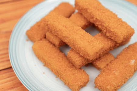 Fried fish sticks on the plate above wooden background.
