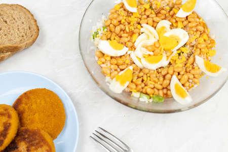 Cooked beans salad with fishcakes and bread served on the table.