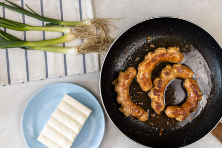 Fried sausages with young onions and white cheese on the plate.