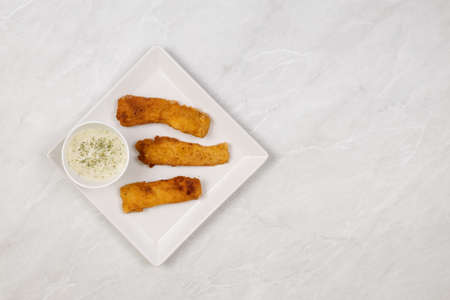 Flat lay above fried chicken meat with dill sauce above white marble background.