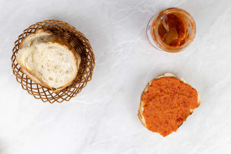 Paprika spread ajvar on the bread above grey marble table.