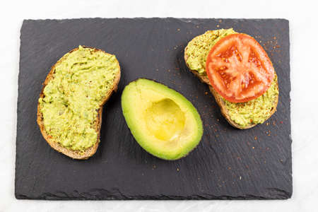 Avocado spread with grated chilly peppers and sliced tomato on the sliced toasted bread.